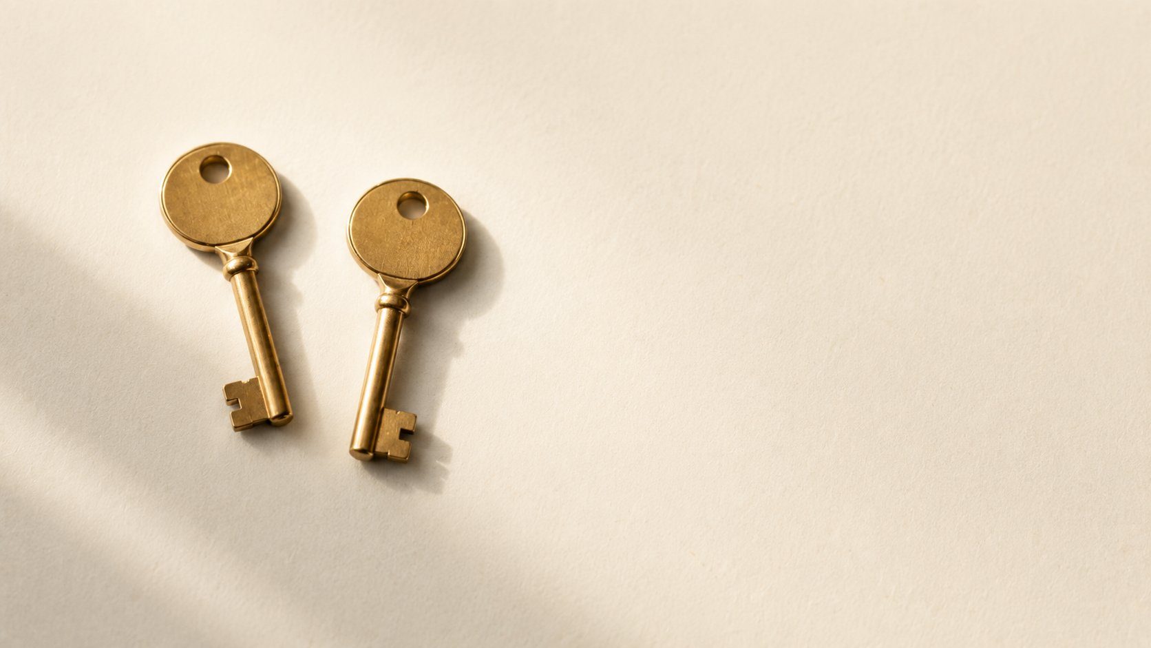 Two near-identical brass keys side by side on a cream surface, a metaphor for one role with two names