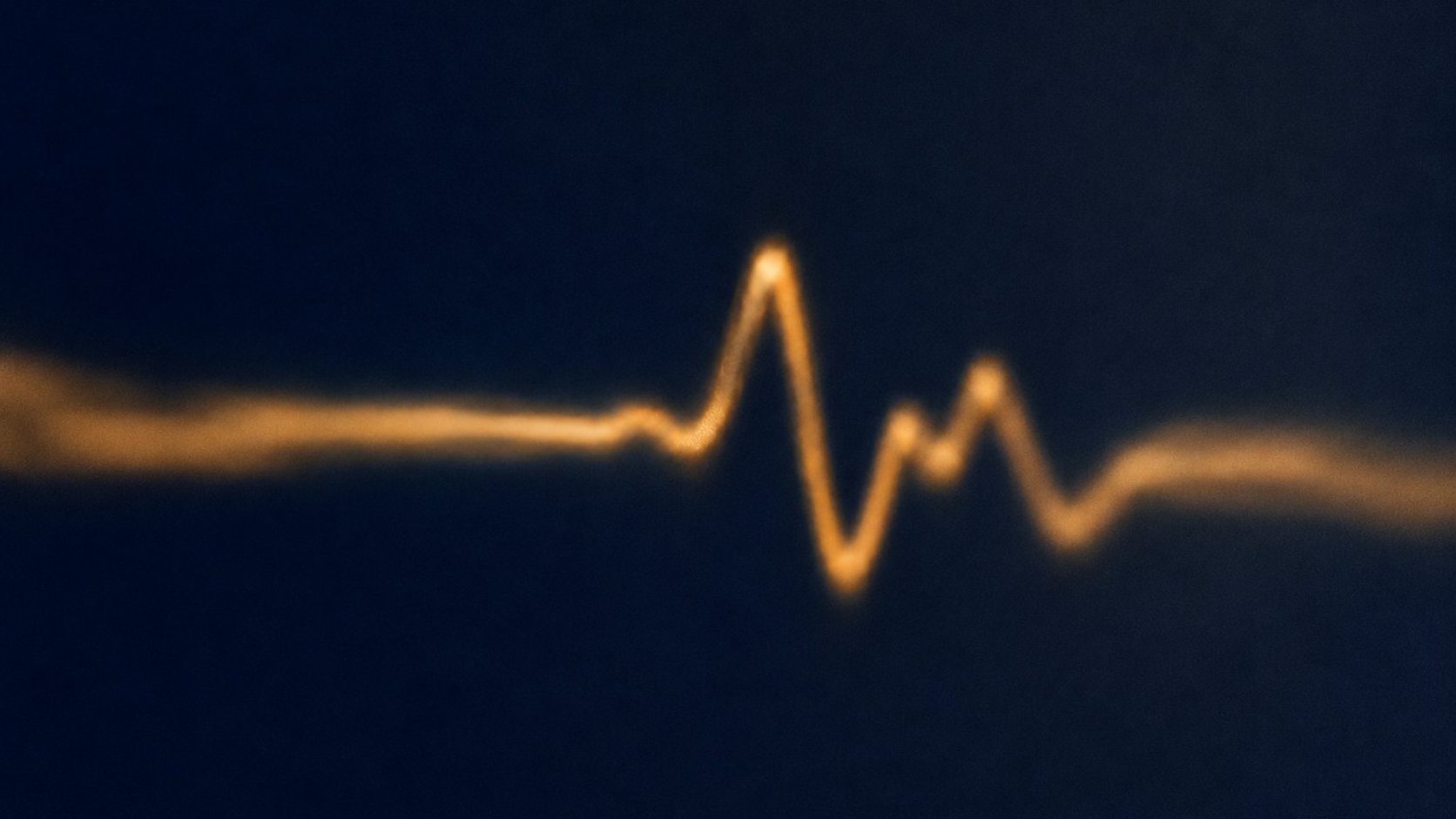 A soft glowing amber monitor trace drifting across a deep navy background, evoking continuous patient monitoring